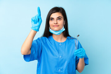 Young woman dentist holding tools over isolated blue background touching on transparent screen