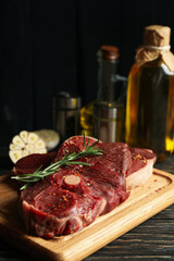 Spices, oil and board with raw steak meat on wooden background