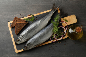 Board with herring fish and spices, and oil on dark wooden background