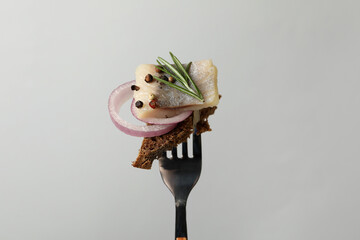Fork with herring fish, bread and spices on light gray background