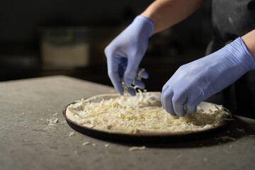 Chef's gloved hands place grated cheese on a round vegetarian pizza. Ingredients in a pizzeria. Italian food concept.
