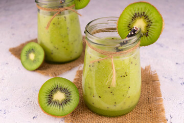 Two healthy fresh kiwi smoothies in jars on a gray background.