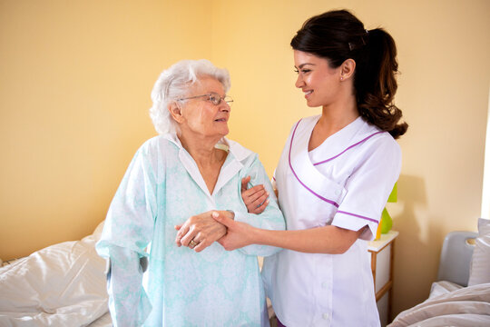 Two women teamwork, lady doctor holding senior woman resident by her arm helping her