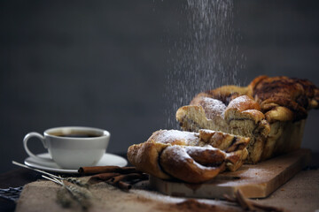 one twist cinnamon bread with one cup of black coffee with chocolate slices and a small bowl of flour on a wooden table