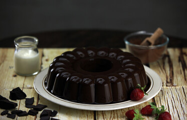 plate of chocolate pudding with strawberries and chocolate slices on the background of a small bottle of milk and a small bowl of cocoa powder on a wooden table