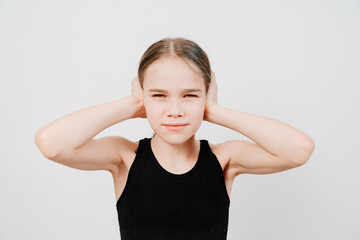 A teen girl with collected hair in a black T-shirt stands on a white background, covers his ears...