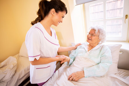 Nursing home doctor holding a hand of a senior woman patient occupant while she is lying