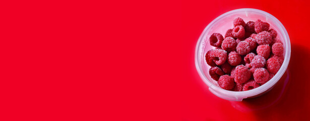banner Berries of Frozen raspberries in a plastic container container on a red background. frozen food concept. Top flat lay view.