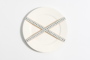  diet, white measuring tape crossed across empty white plate, white background