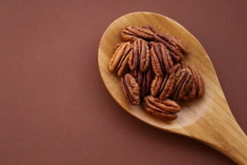 Pecan nut close-up in wooden spoon on bright brown background.Healthy fats.Heap shelled Pecans nut closeup. Ingredient of the keto diet.Tasty raw organic food and healthy snack
