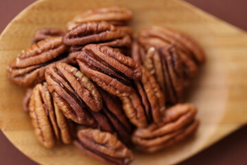 Pecan nut close-up in wooden spoon on bright brown background.Healthy fats.Heap shelled Pecans nut closeup. Ingredient of the keto diet.Tasty raw  food and healthy snack