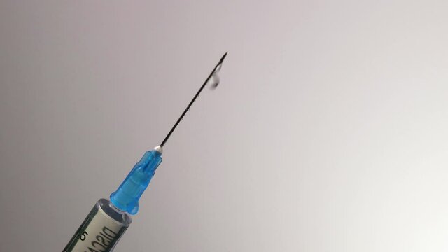 Injection drops are dripped from a sharp needle on a medical syringe. Shooting close-up on a gray background