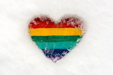 a small heart painted in rainbow colors lies on the snow. Close-up