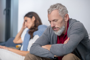 Upset bearded man sitting near his wife after an argument