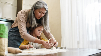 Grandmother cutting cookies from dough with little granddaughter