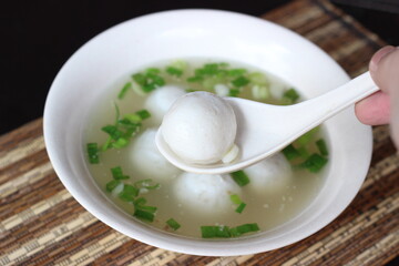 a bowl of soup with white meatball and white spoon