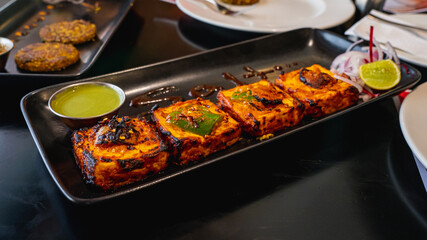 Selective focus of Paneer Tikka Kebab served with green chutney on a black serving tray. White...