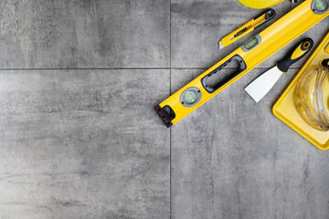 Contractor concept. Tool kit of the contractor: yellow hardhat, libella, hand saw on the gray tiles background.