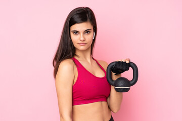 Young sport woman over isolated pink background making weightlifting with kettlebell