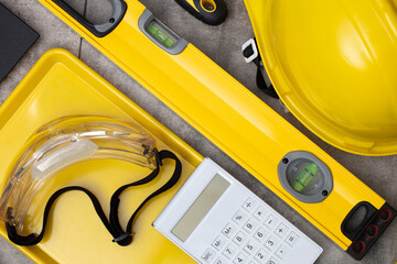Contractor concept. Tool kit of the contractor: yellow hardhat, libella, hand saw on the gray tiles background.