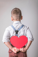 Boy holding a red heart  .behind the back, symbol of love, family, hope. Backgrounds for cards on Valentine's Day or social posters about the preservation of the family and children.