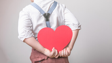 Boy holding a red heart  .behind the back, symbol of love, family, hope. Backgrounds for cards on Valentine's Day or social posters about the preservation of the family and children.