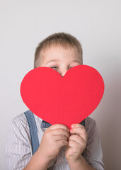 Five year old smiling boy holding a red heart  symbol of love, family, hope. Backgrounds for cards on Valentine's Day or social posters about the preservation of the family and children.