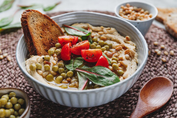 Hummus with green pea, pine nuts, tomatoes and swiss chard. Vegetarian healthy dish, top view.