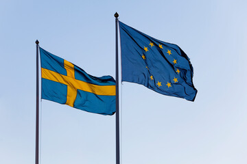 The Swedish and EU flag waving in the wind. lear light blue sky in background.