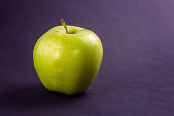 Side view of a fresh green apple on a dark textured surface. Copy space