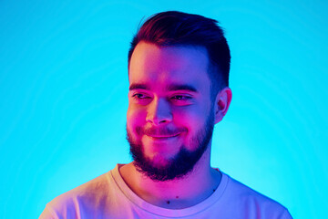Smiling. Caucasian man's portrait isolated on blue studio background in neon light. Beautiful male...