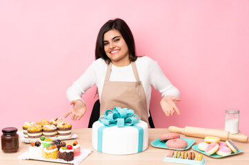 Obraz na płótnie Canvas Pastry chef with a big cake in a table over isolated pink background smiling