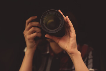 Private detective with camera spying against black background, focus on lens