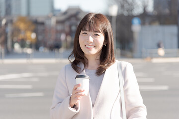 Fototapeta premium オフィス街でコーヒーカップを持って歩く女性