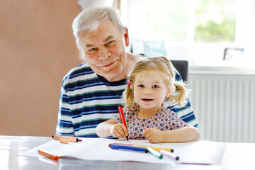 Cute little baby toddler girl and handsome senior grandfather painting with colorful pencils at...