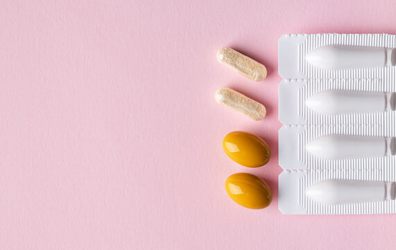 Vaginal suppositories on pink background. Top view. Copy space. Vulvovaginal infections treatment. Gynecological medicines for womens health in form of suppository, capsules and oval shaped pill. 