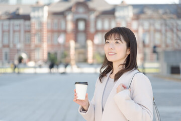 Fototapeta na wymiar 東京駅でコーヒーを持って歩く女性