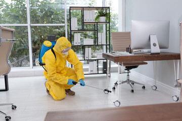 Janitor in protective suit disinfecting office to prevent spreading of COVID-19
