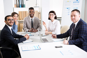 Multy-ethnic group of business people working while sitting at the office desk and smiling at camera