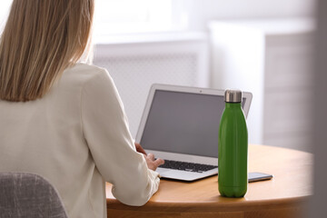 Woman with thermo bottle working at table in modern office, closeup
