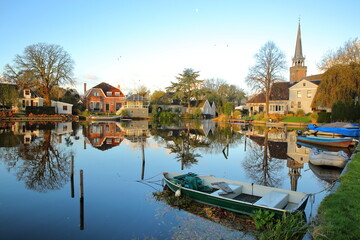 Broek in Waterland, a small town with traditional old and painted wooden houses, North Holland, Netherlands, with reflections of the houses and the church, and colorful wooden boats in the foreground