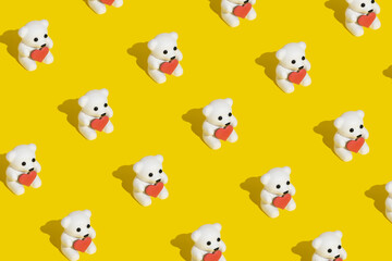 Pattern made with white teddy bears holding a heart shaped cookie on modern trendy yellow background. Minimal Valentines, romantic or love concept. Copy space.