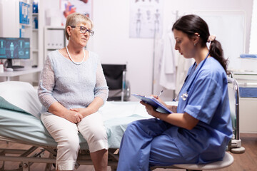 Obraz premium Nurse writing prescription on clipboard discussing with senior man. Elderly patient having a converstation with medical stuff in private clinic during consultation.