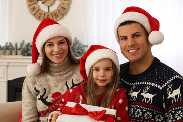 Happy family in Santa hats at home. Daughter holding Christmas present