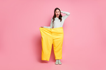 Full size portrait of shocked person hand on head open mouth too big old pants isolated on pink color background