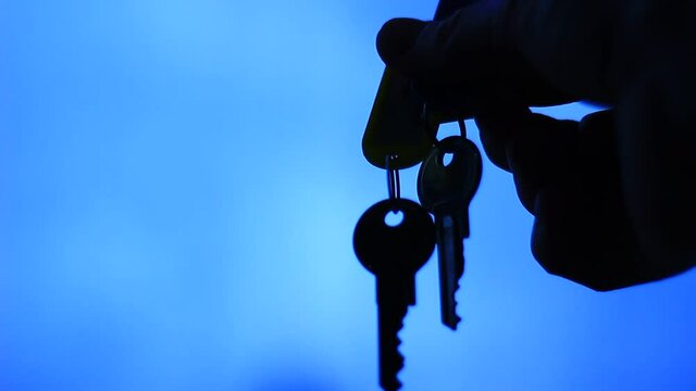 Holding keys between fingers, dark room, against light in the back. Only silhouettes visible.