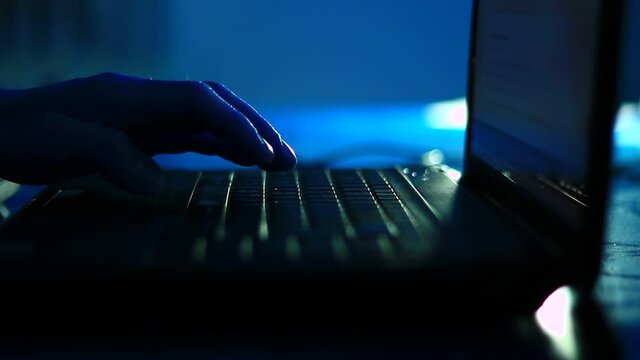 Typing on the laptop keyboard in the dark room, office. Close up, point to fingers.