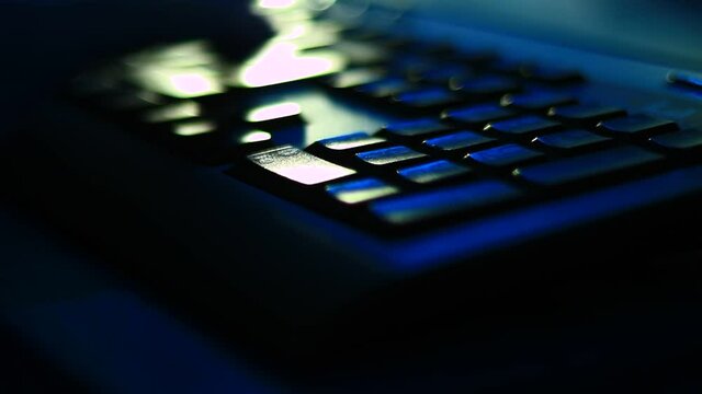 Typing on the laptop keyboard in the dark room, office. Close up, point to fingers.