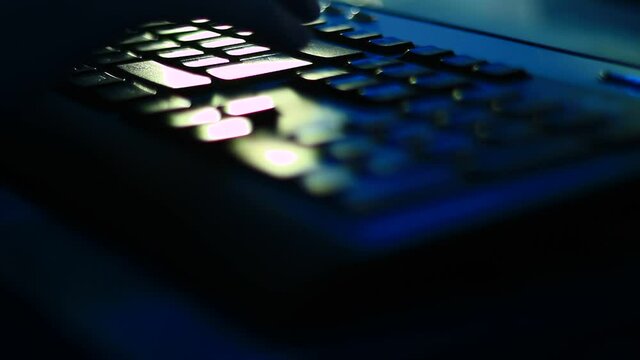 Typing on the laptop keyboard in the dark room, office. Close up, point to fingers.