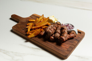 Kebabs served with french fries on wooden board